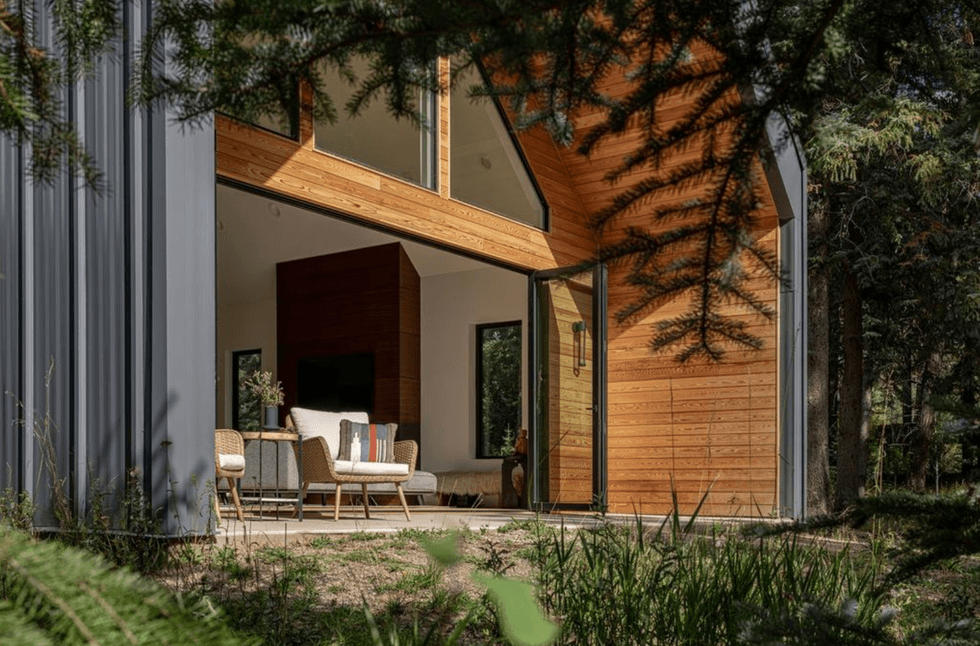 Modern cabin with open patio, surrounded by trees and sunlight streaming in.