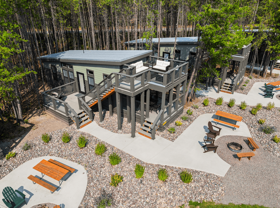 Modern cabins with decks, picnic tables, and a fire pit set in a forested area.