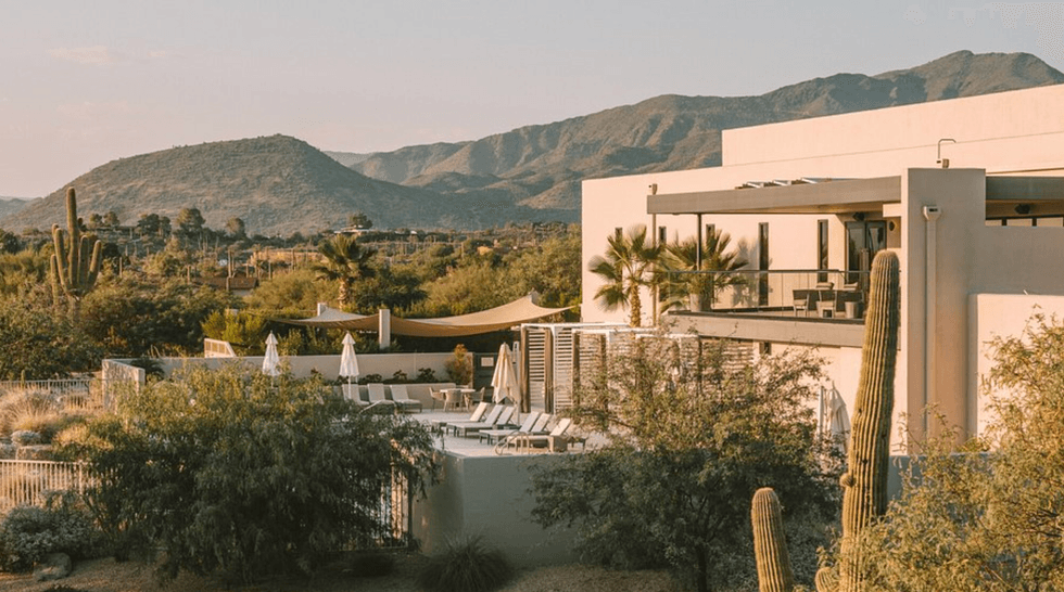 Modern desert house with mountains, cacti, pool, and sunlit patio.