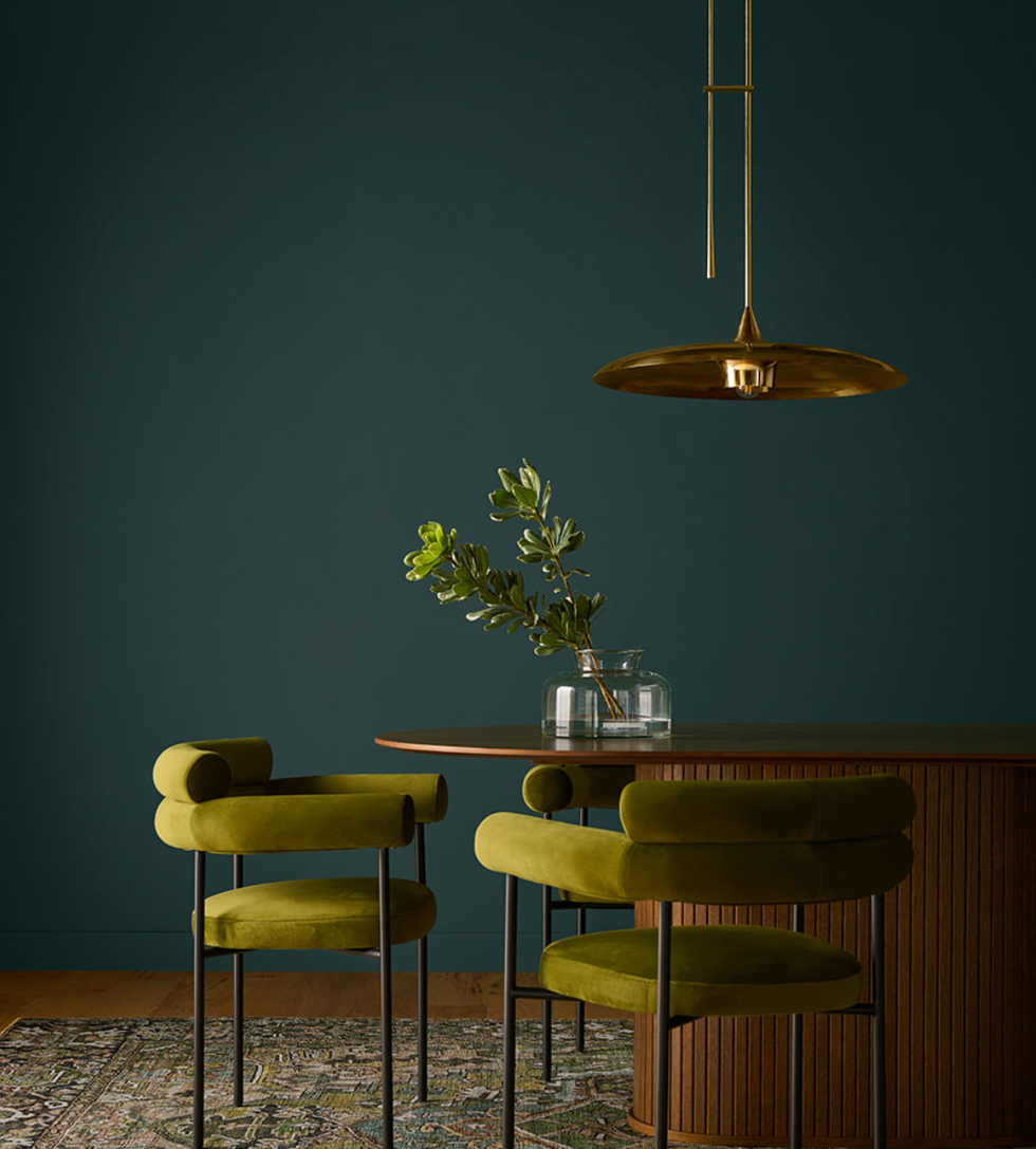 Modern dining room with green chairs, wooden table, gold pendant light, and a vase of plants.