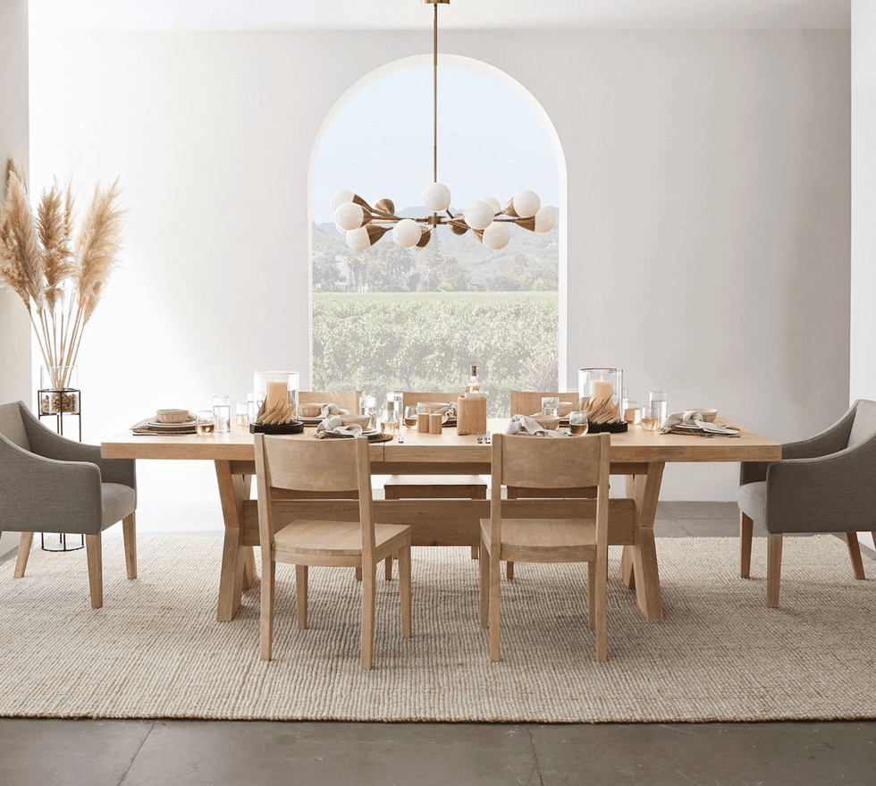 Modern dining room with wooden table, six chairs, pampas grass, and large window view.