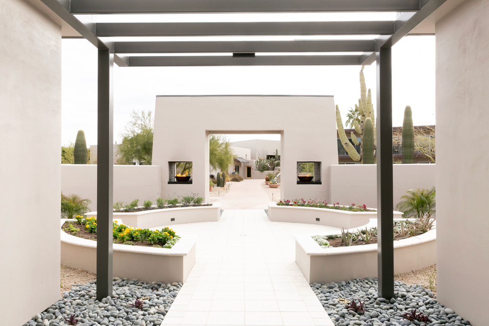 Modern garden courtyard with cacti, planters, and a pergola pathway under a cloudy sky.