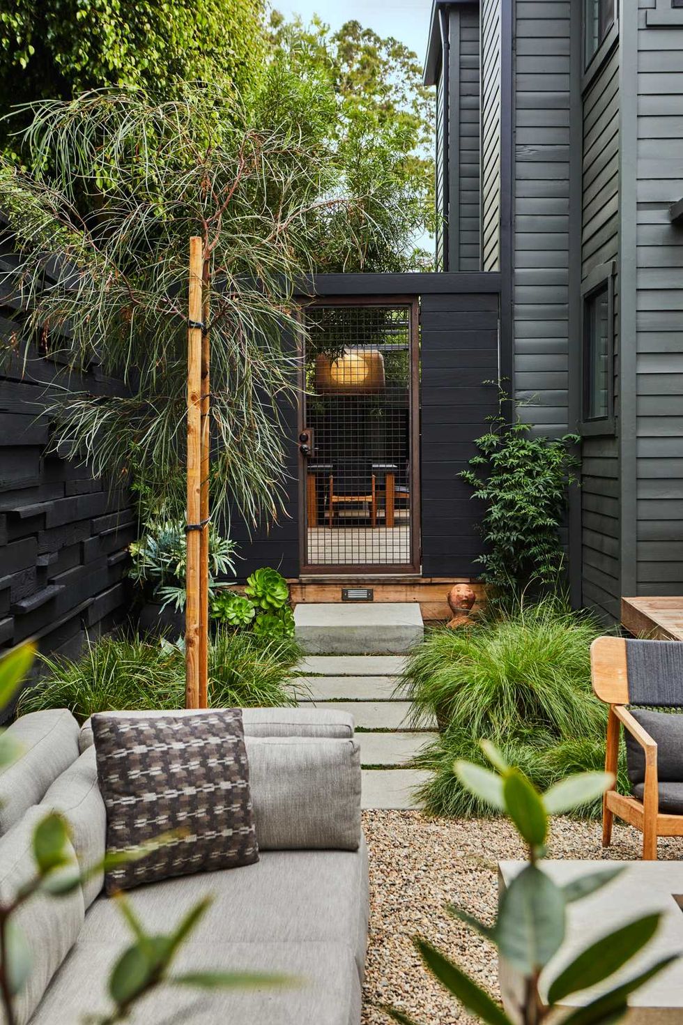 Modern garden patio with gray sofa, stone path, and lush greenery.