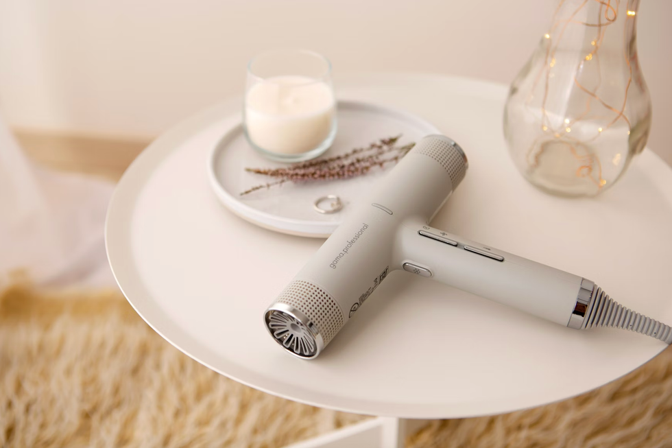 Modern hairdryer on white table with candle and decorative vase.