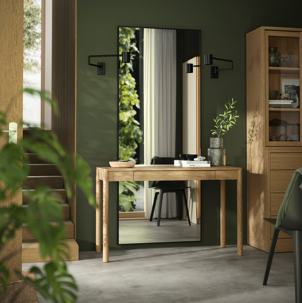 Modern hallway with a wooden table, mirror, and wall-mounted lights in a green-themed room.