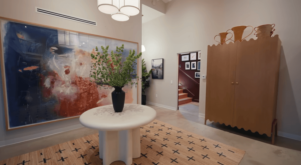 Modern hallway with abstract art, round table, and decorative cabinet.