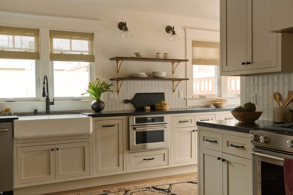 Modern kitchen with beige cabinets, black countertop, and farmhouse sink under window.