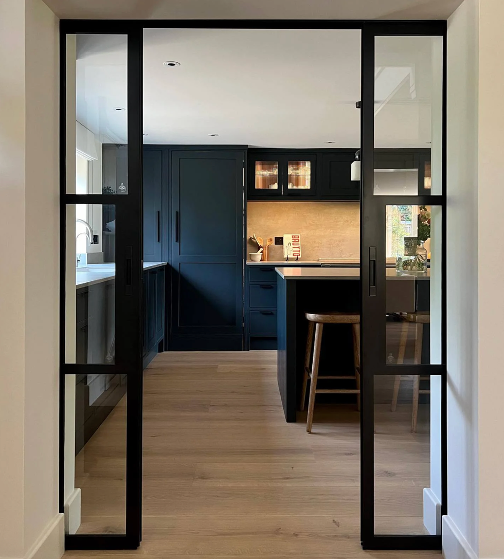 Modern kitchen with black cabinets and large glass doors, wooden floor, and island stool.