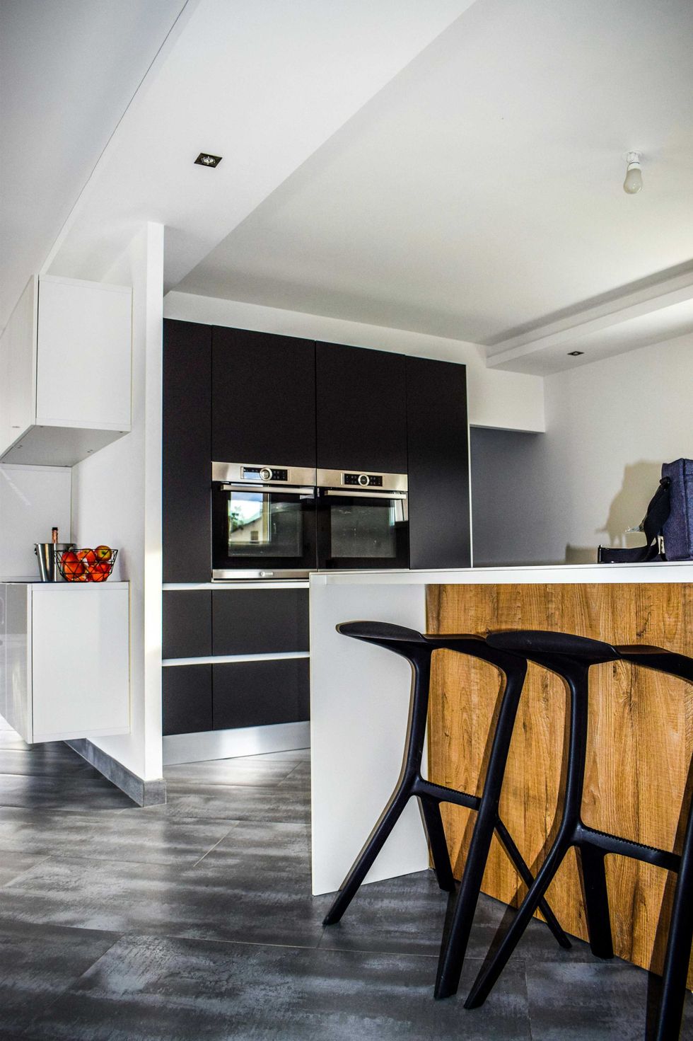 Modern kitchen with black cupboards, a wooden island, and sleek black bar stools.