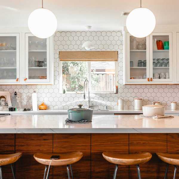 Modern kitchen with hexagonal tiles, wooden stools, and pendant lights over an island.