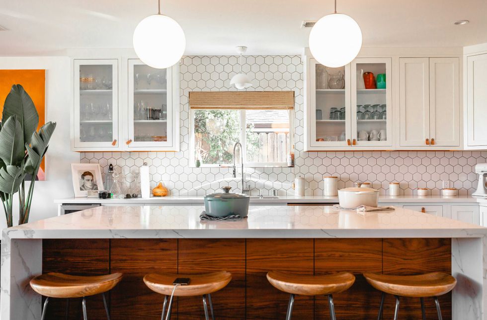 Modern kitchen with hexagonal tiles, wooden stools, and pendant lights over an island.