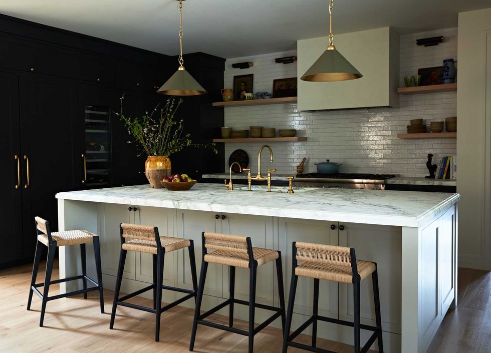 Modern kitchen with island, wicker stools, marble countertop, and pendant lights.