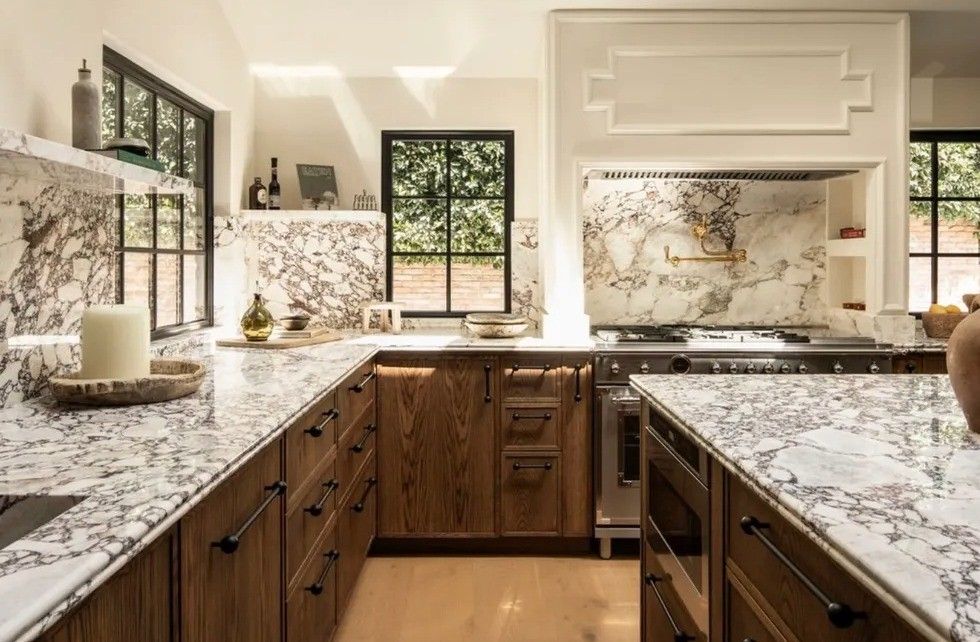 Modern kitchen with marble countertops, wooden cabinets, and large windows.