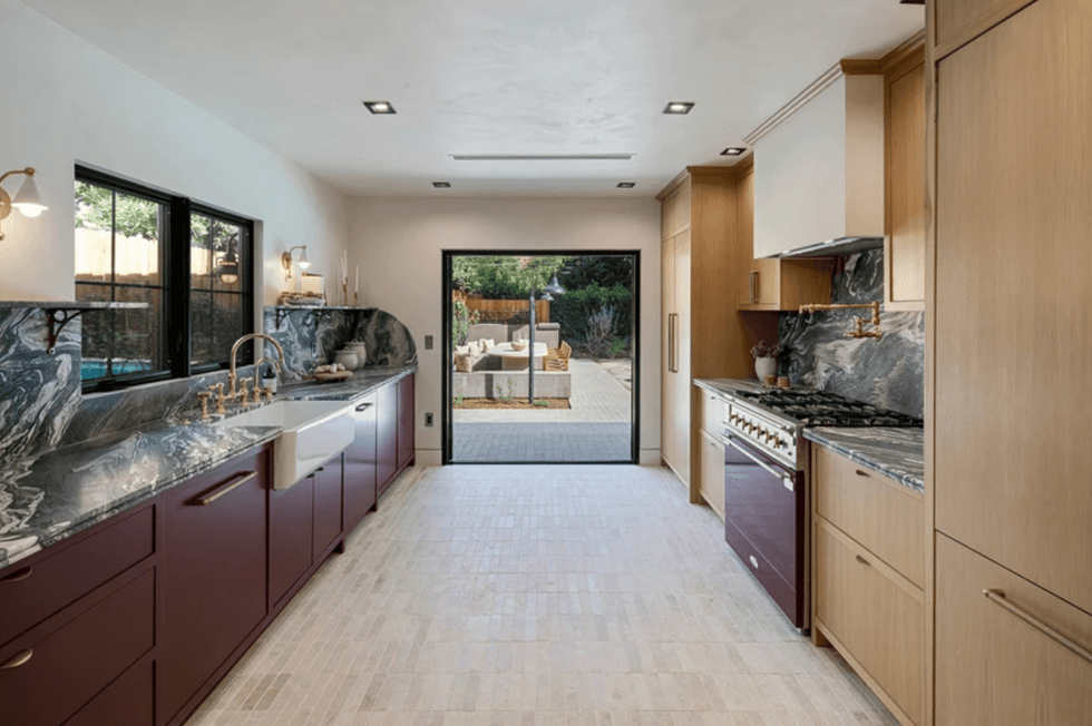 Modern kitchen with marbled countertops, gold fixtures, and glass doors opening to a patio.