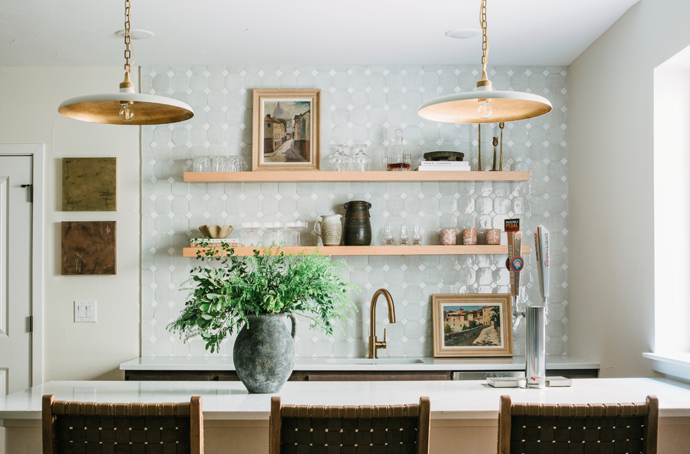 Modern kitchen with open shelves, framed art, and a large plant vase on the counter.