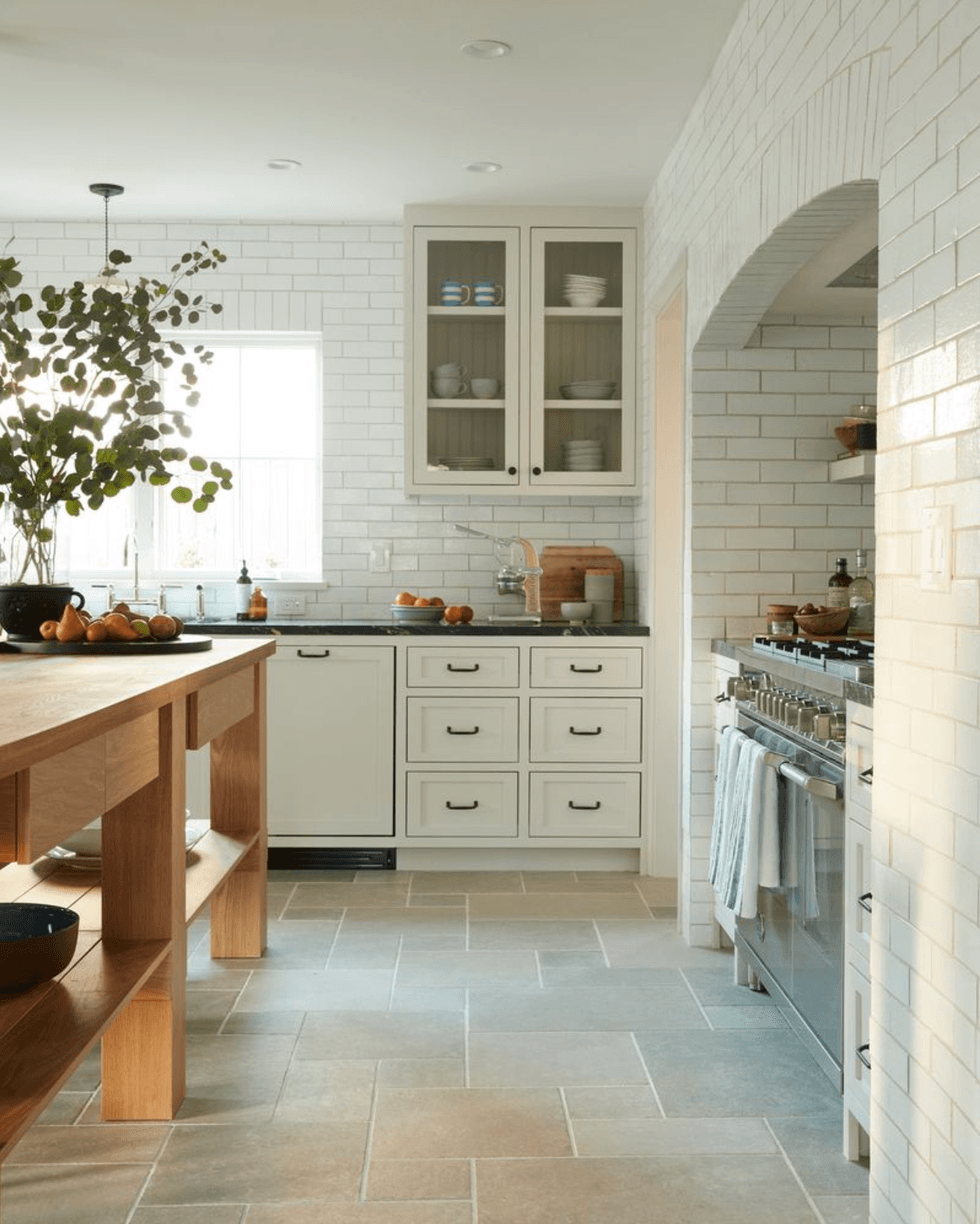 Modern kitchen with white cabinets, a wooden island, and potted greenery by a window.