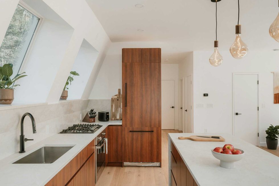 Modern kitchen with wood cabinets, island, skylights, and hanging bulbs.