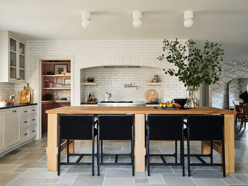 Modern kitchen with wood island, black chairs, white subway tiles, and greenery.