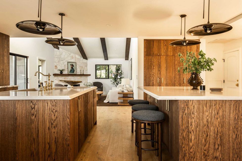 Modern kitchen with wooden cabinets, island, black pendant lights, and green plant decor.