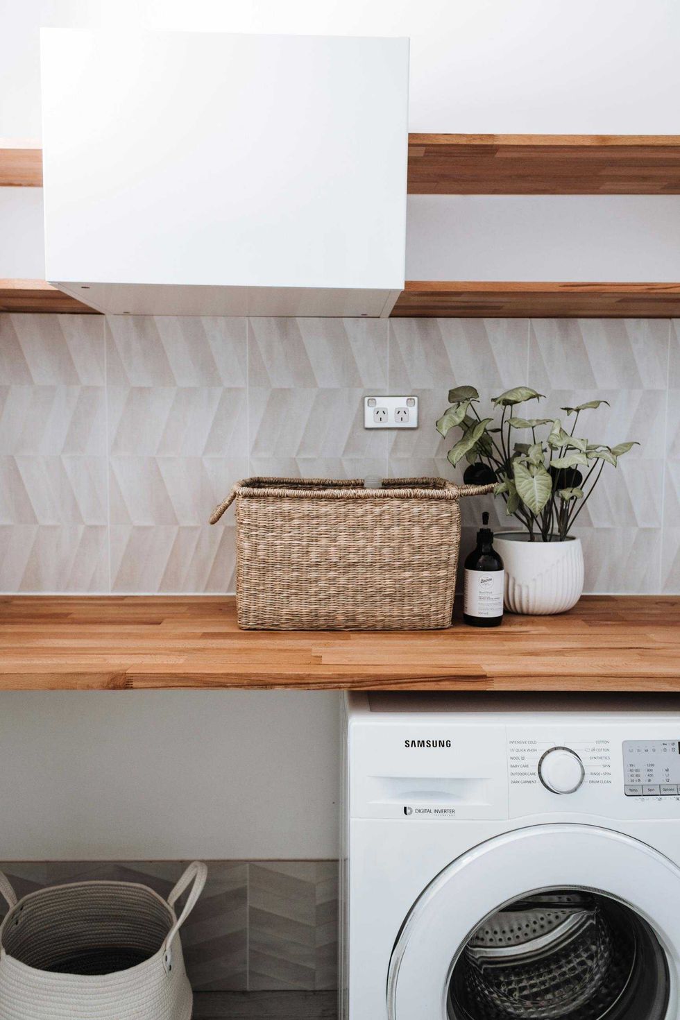 Modern laundry room with wooden shelves, washing machine, and potted plant.