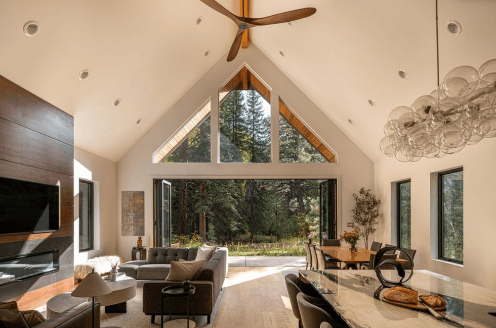 Modern living room with large windows, forest view, and elegant furnishings.