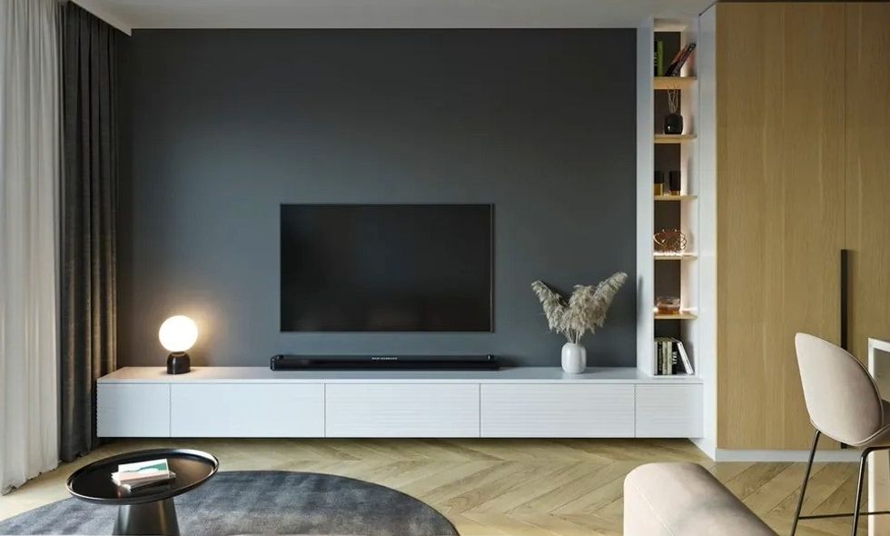 Modern living room with TV, dark accent wall, white cabinet, lamp, and shelves.