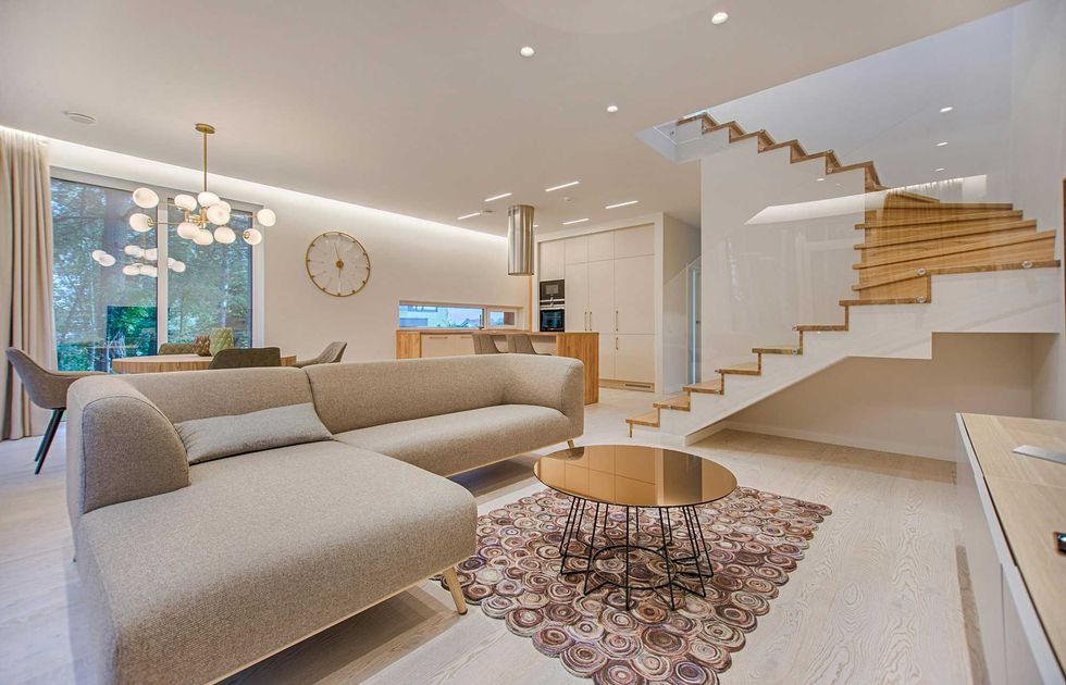 Modern open living space with a beige sofa, wooden stairs, and circular chandelier.