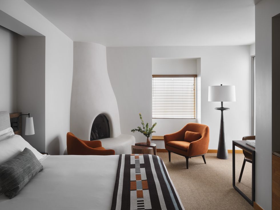 Modern room with bed, fireplace, orange chairs, and tall lamp by a window.