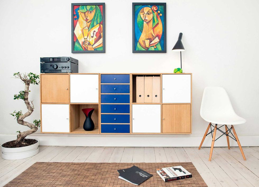 Modern room with colorful art, a wooden cabinet, stereo, white chair, and small bonsai tree.