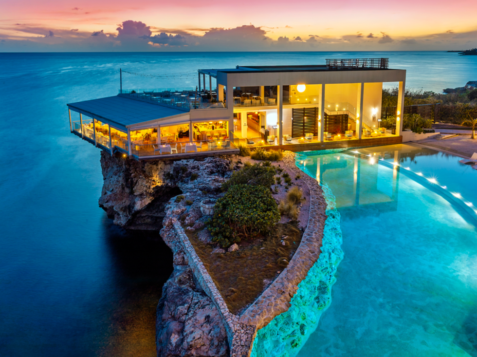 Modern seaside house on a rocky cliff, overlooking ocean at vibrant sunset.