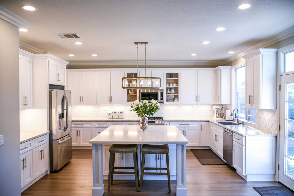 Modern white kitchen with island, stainless steel appliances, and hanging lights.