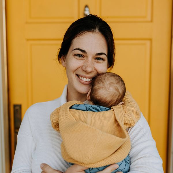 mom standing in front of yellow door while holding newborn