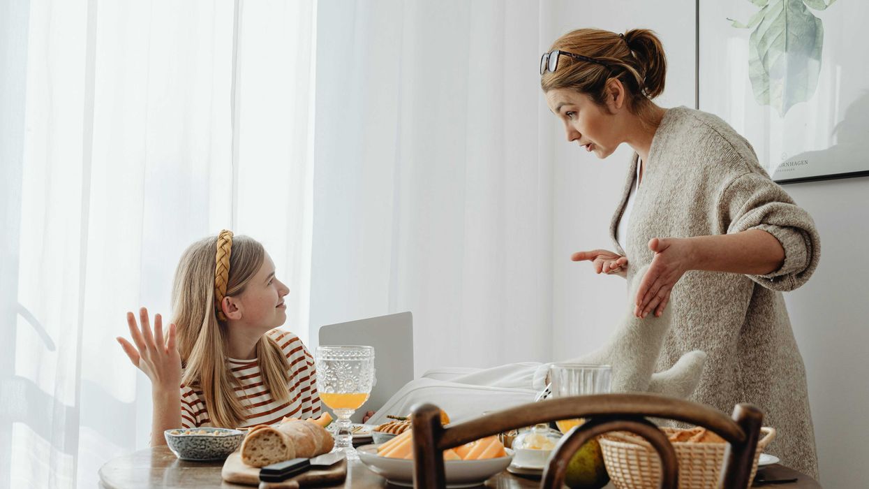Mother and daughter having a discussion at breakfast table with bread and fruits.