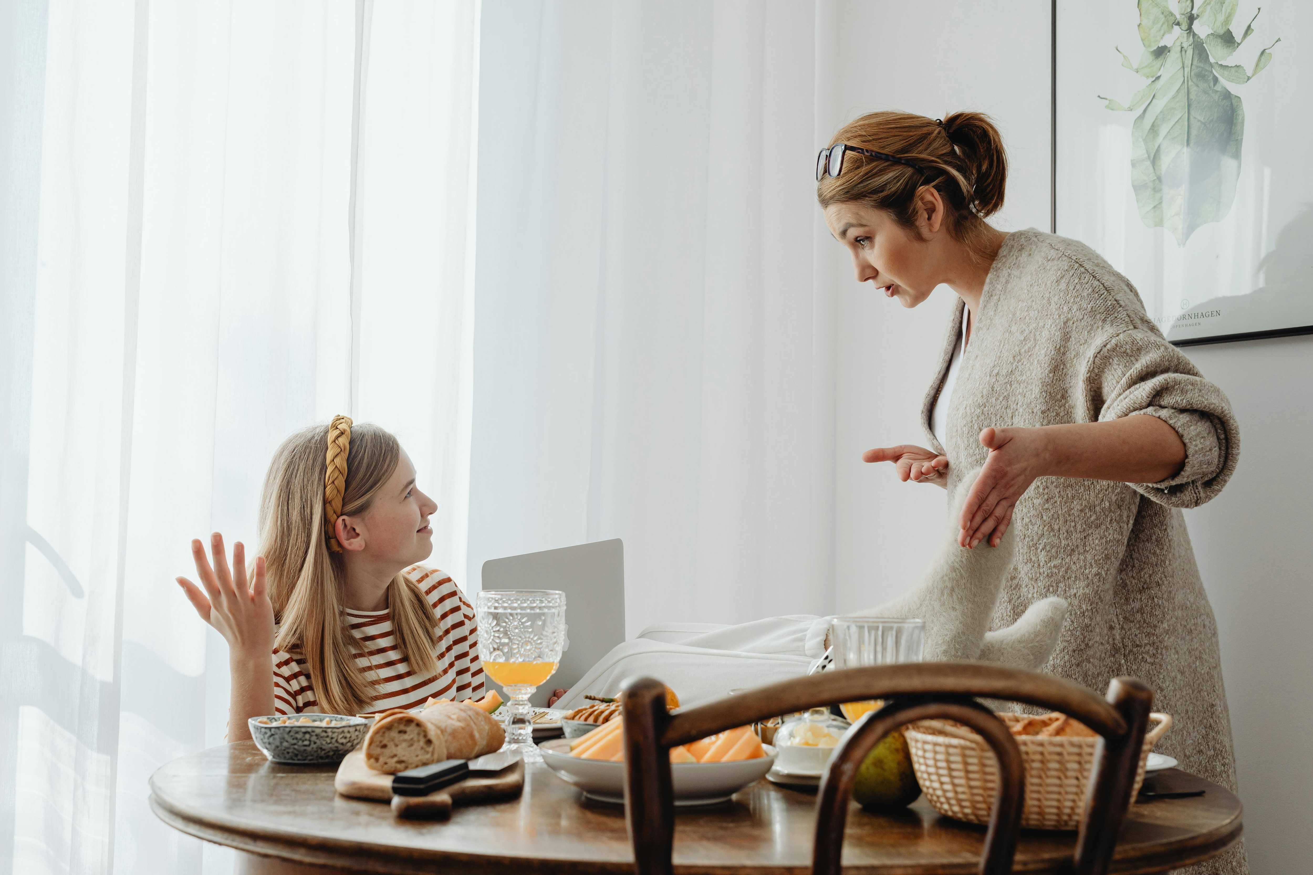 Mother and daughter having a discussion at breakfast table with bread and fruits.