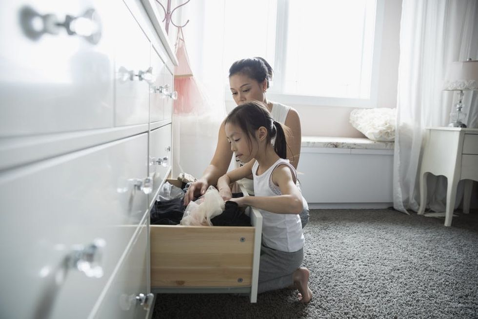 Mother and daughter putting laundry away in dresser drawer in bedroom
