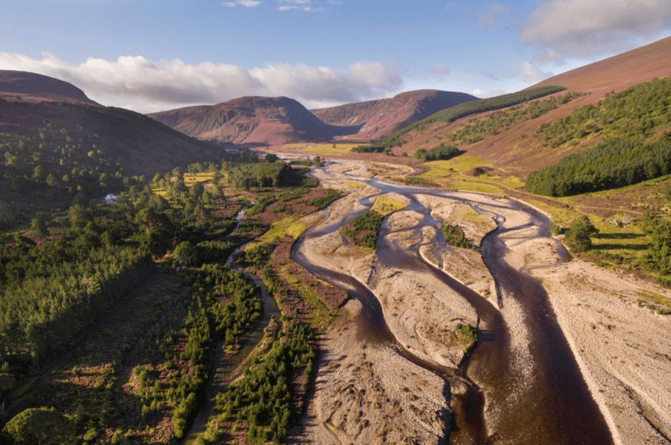 Mountain valley with a meandering river and lush greenery under a blue sky.