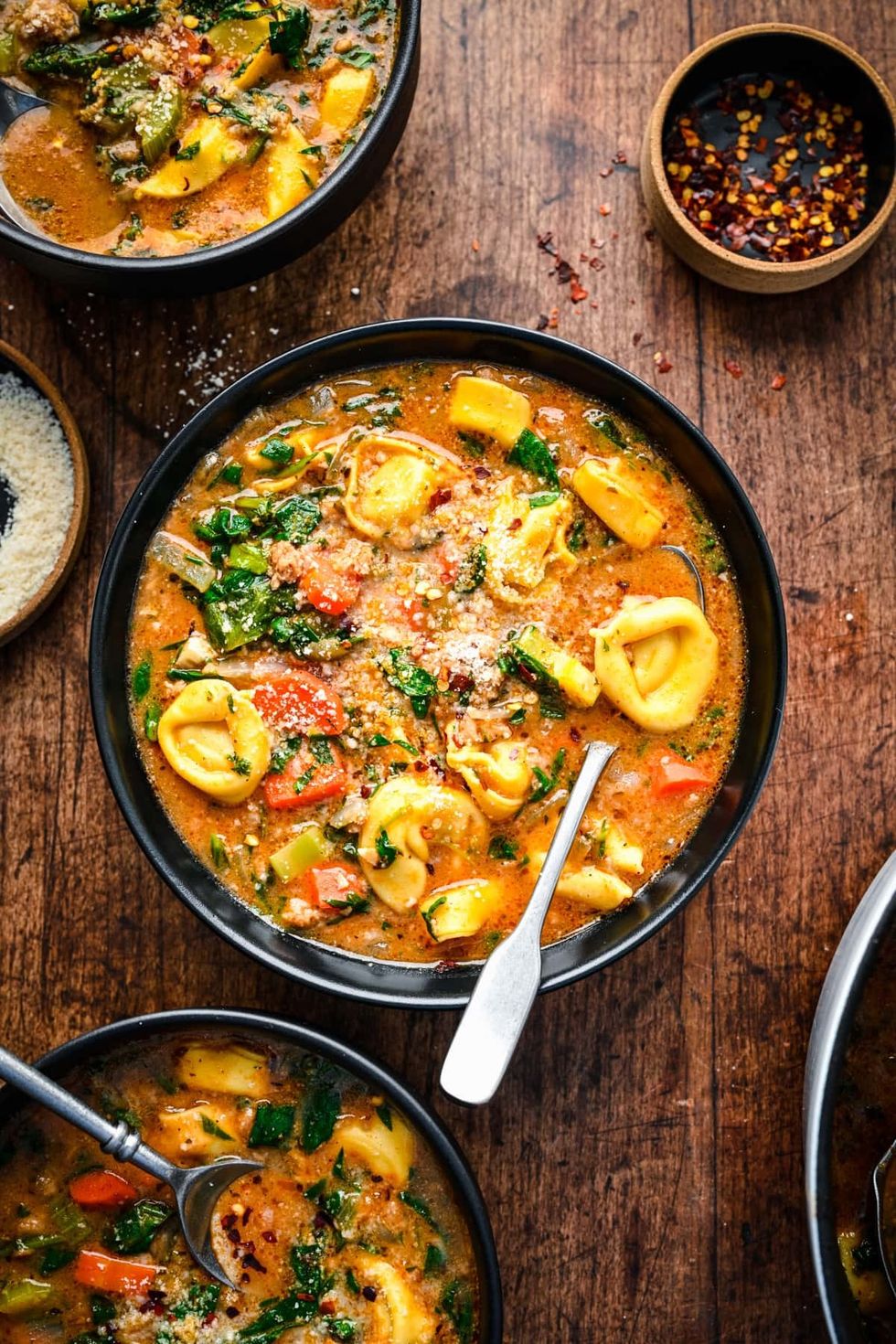 Multiple bowls of vegan tortellini soup are sitting on a wooden table.