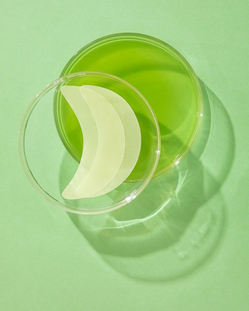 Murad eye patches are in a clear container on top of a green surface.