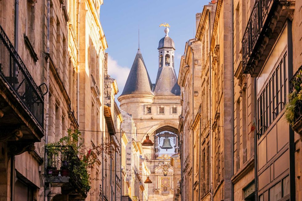 Narrow street view of historical bell tower, framed by old stone buildings under a clear sky.