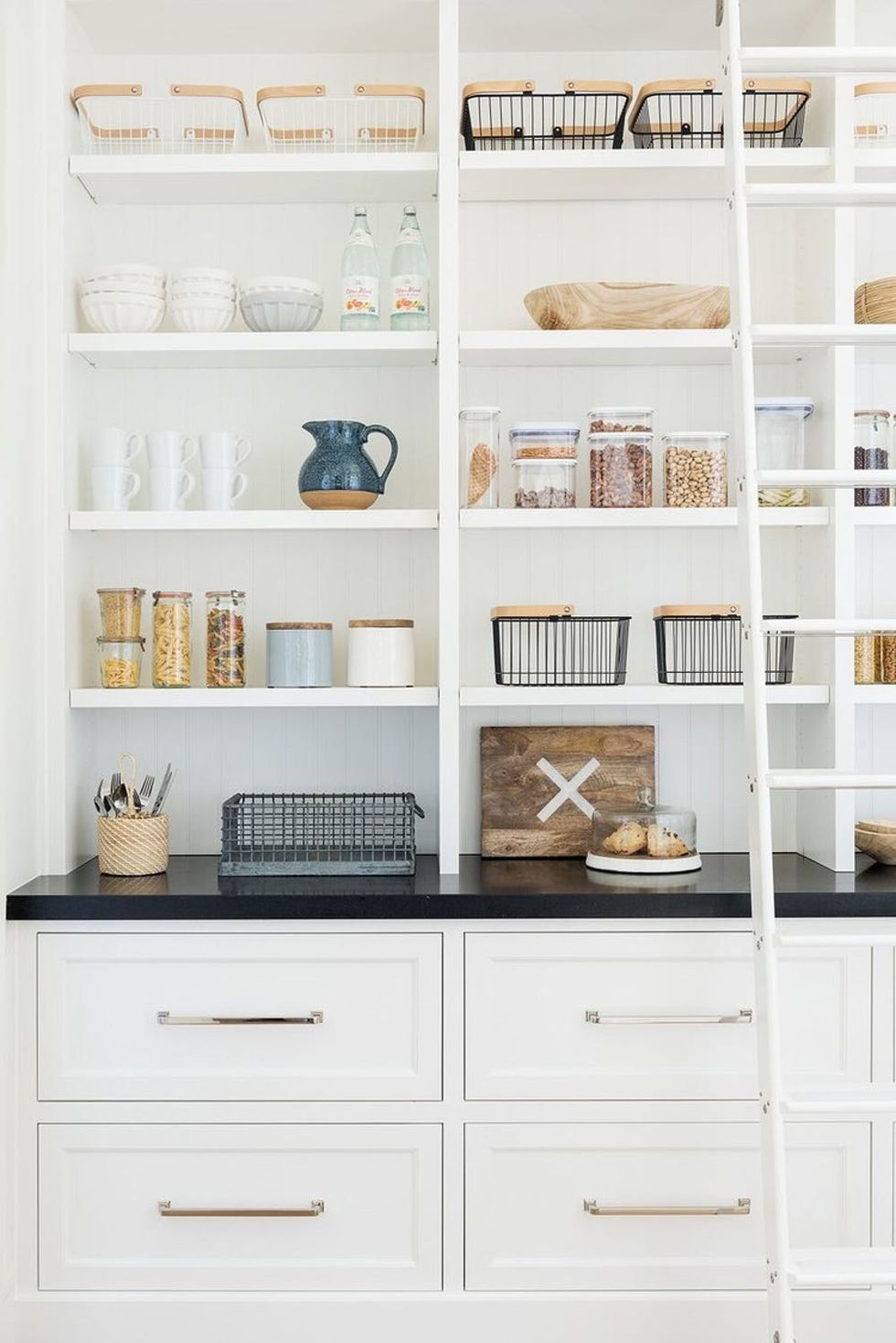 Neat kitchen pantry with shelves of jars, baskets, and dishes, plus a ladder on the right.