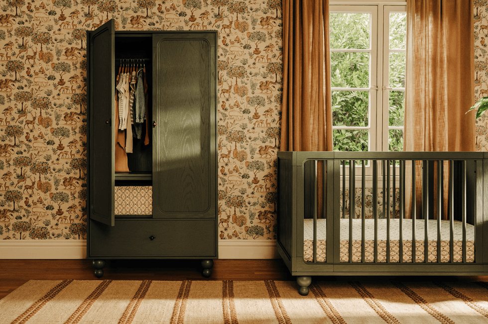 Nursery room with a crib, open wardrobe, animal wallpaper, and a window with brown curtains.