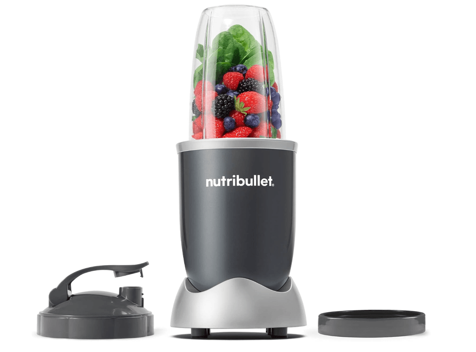 Nutribullet blender with fruits and greens, two lid options beside it.