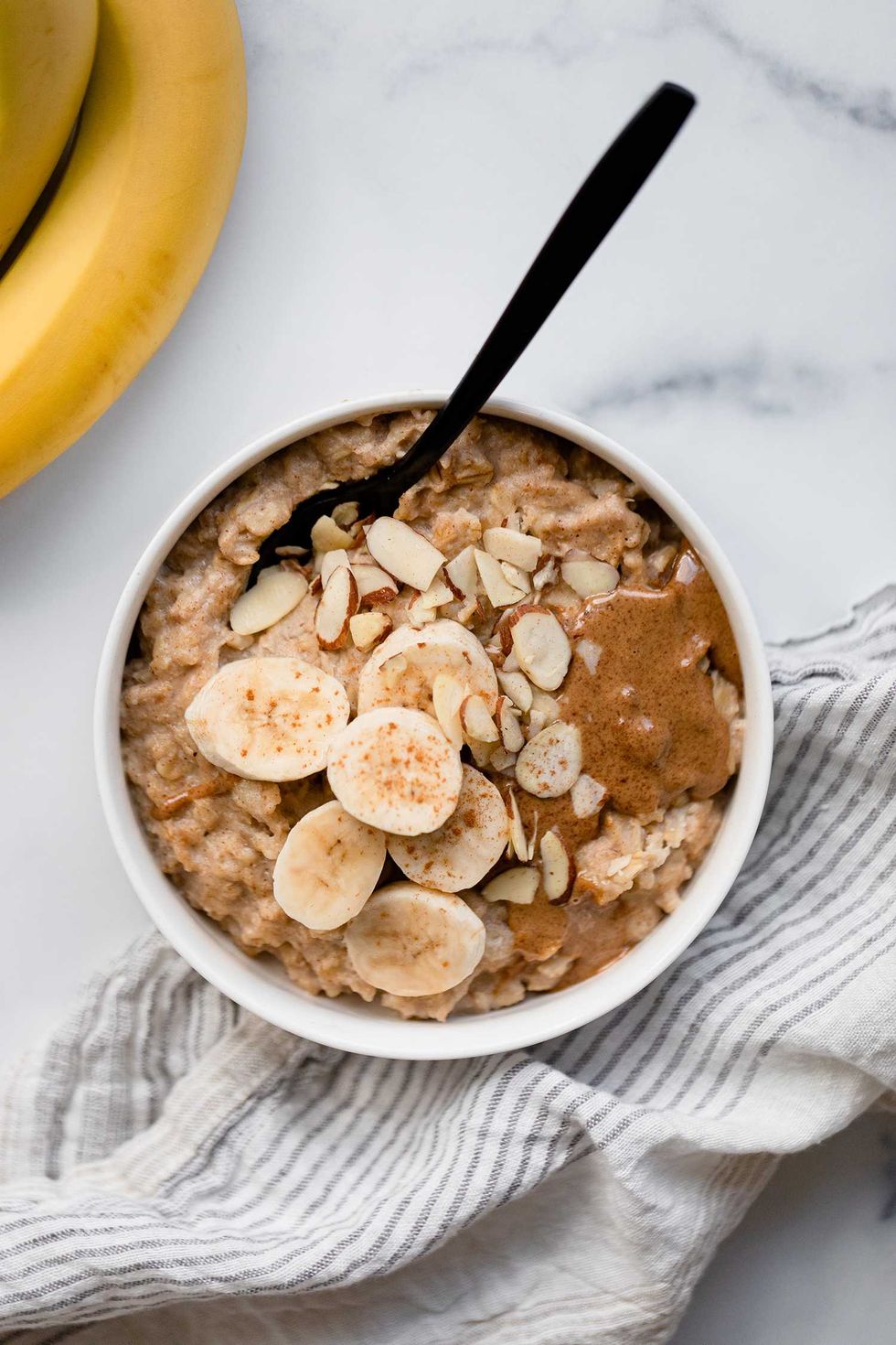 Oatmeal with banana slices, almond slivers, and nut butter in a bowl with a spoon.