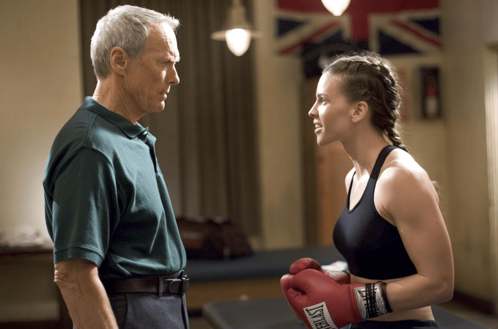 Older man and woman with boxing gloves face each other in a gym.