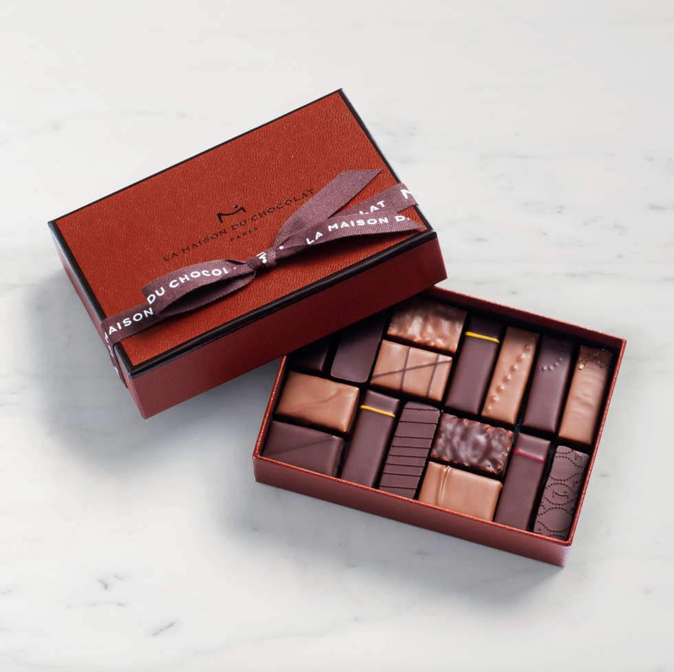 Open chocolate box with assorted chocolates, brown ribbon on the lid.