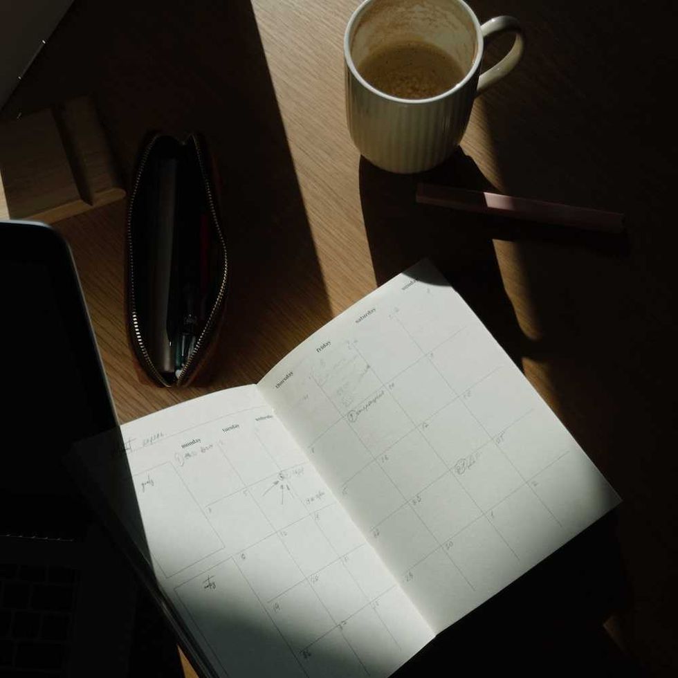 Open planner on a sunny desk with a coffee mug, pen pouch, and laptop.