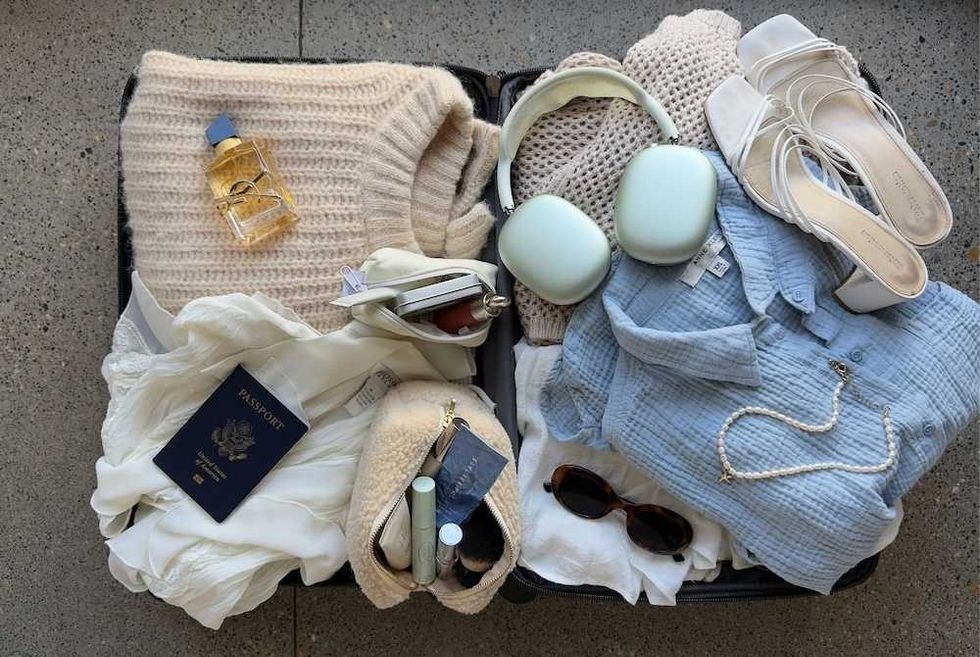 Open suitcase with clothes, headphones, sandals, passport, and toiletries on a textured floor.