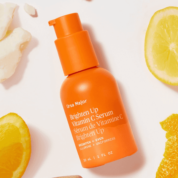 Orange bottle of Ursa Major Vitamin C Serum surrounded by citrus slices.
