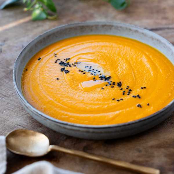 Orange carrot soup in a bowl, garnished with black seeds, with a gold spoon beside it.