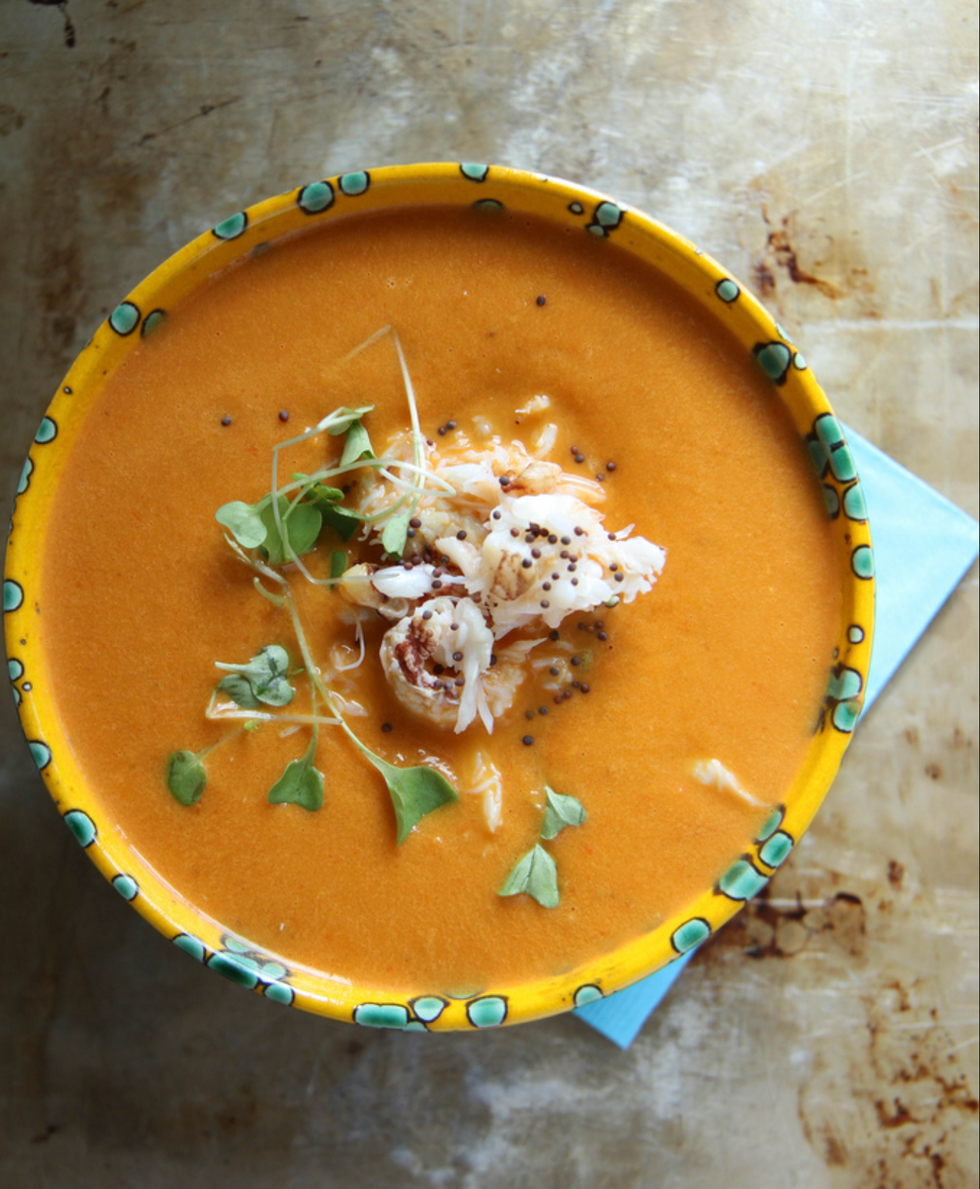 Orange soup in a patterned bowl, garnished with crab, greens, and mustard seeds.